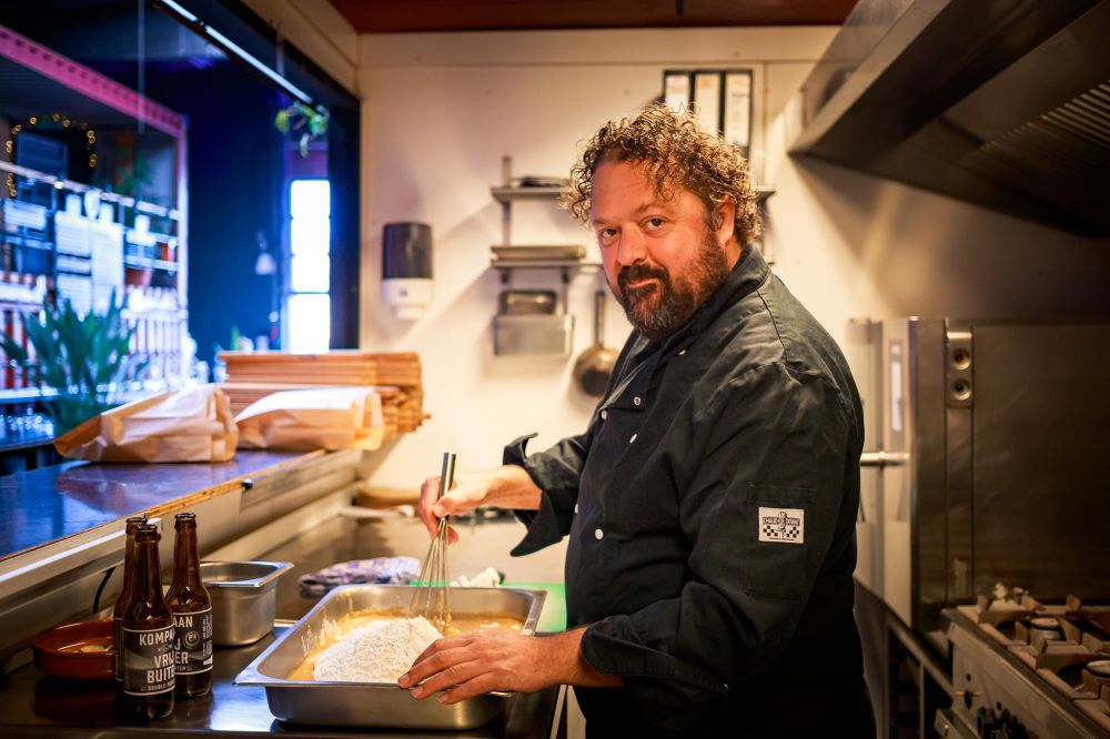 kok in professionele keuken die oliebollen aan het maken is en in camera kijkt