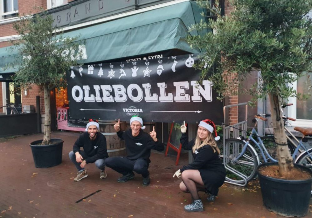 een grote poster met het woord oliebollen waar twee jongens en een meisje onder poseren met twee bomen